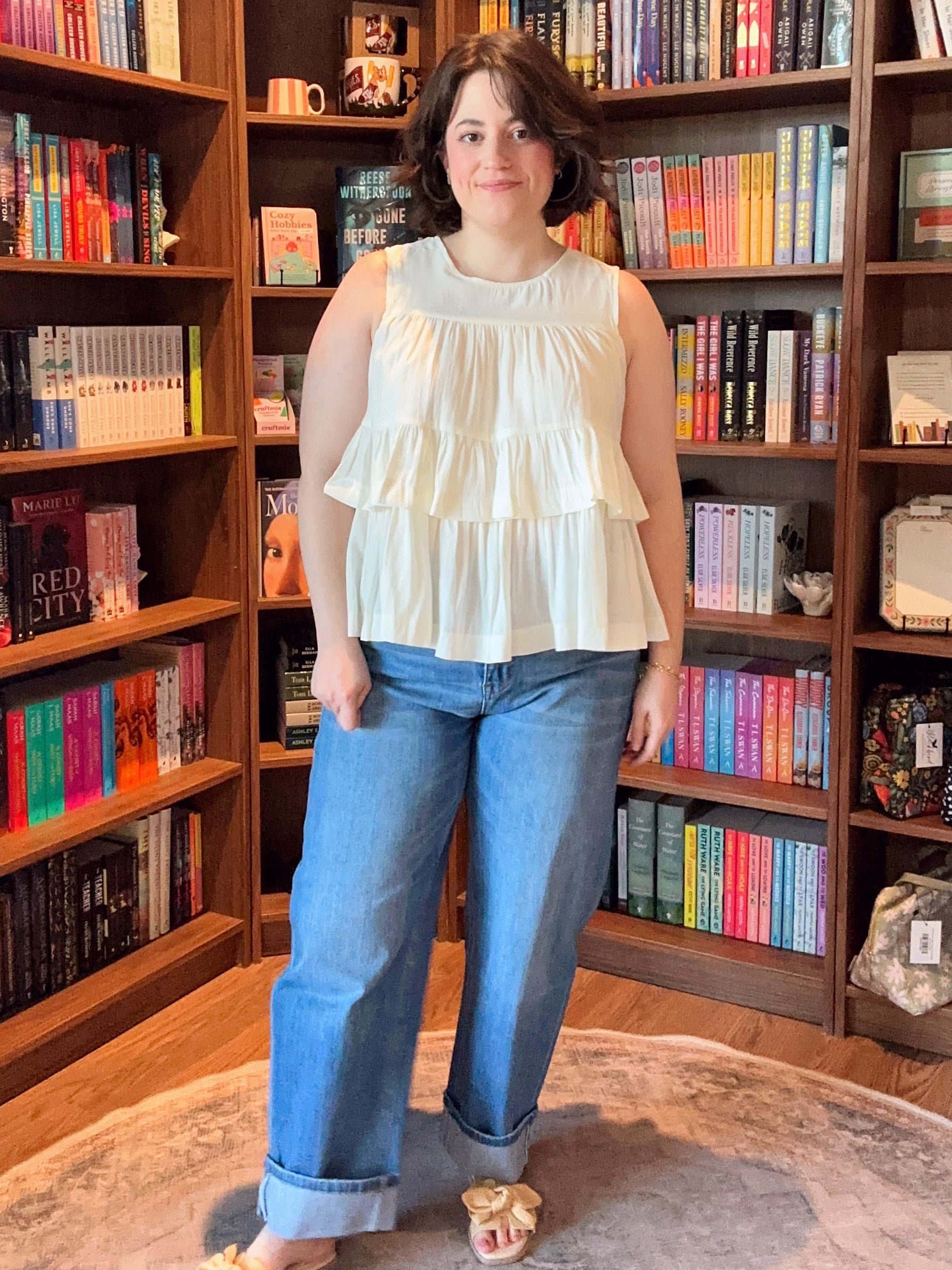 Woman standing in a room with bookshelves filled with books and decorative items.