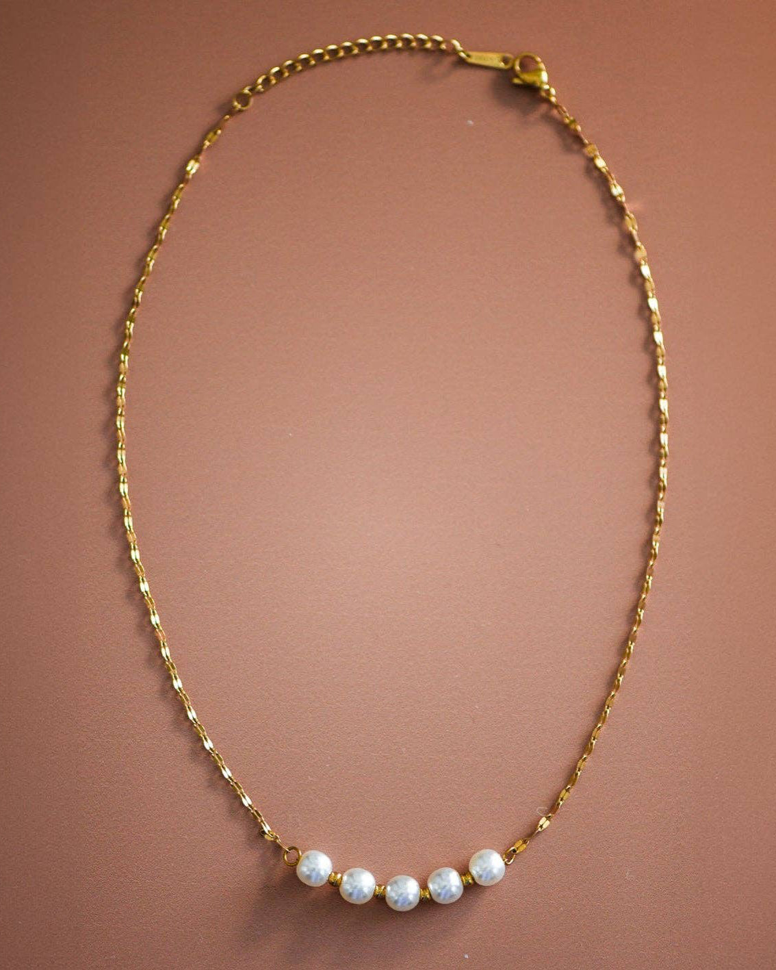 Gold necklace with small pearls on a brown background