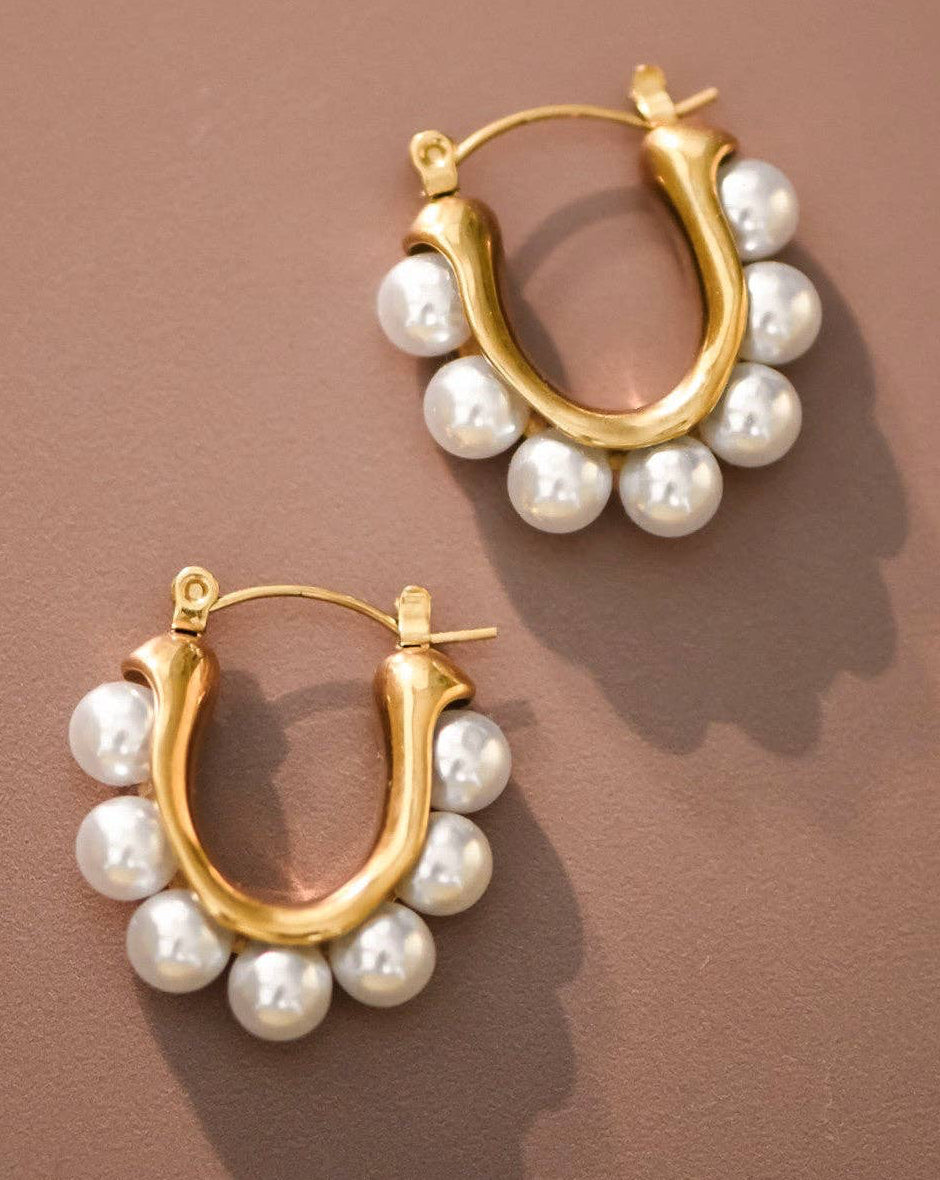 Gold hoop earrings with pearl beads on a brown background