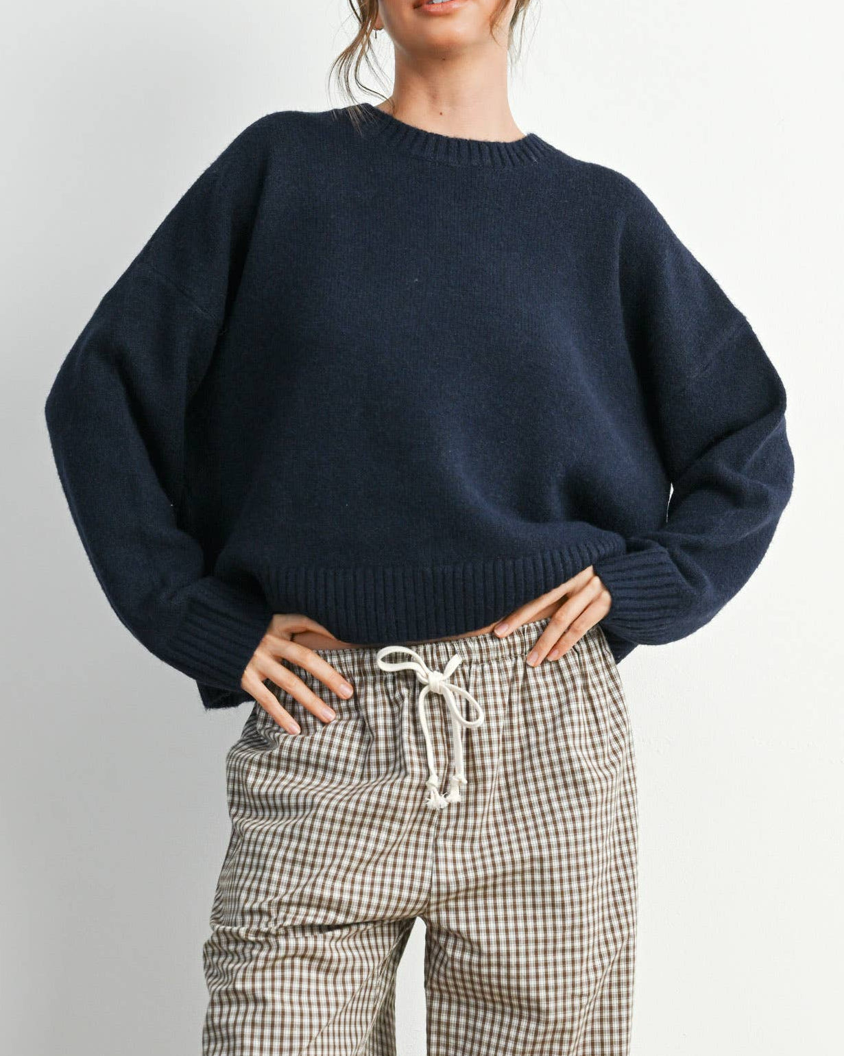 Woman wearing a navy sweater and checkered pants against a white background