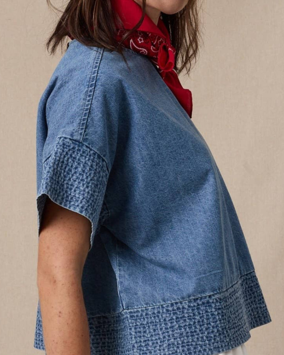 Woman wearing a blue denim top with a red scarf, standing against a beige background