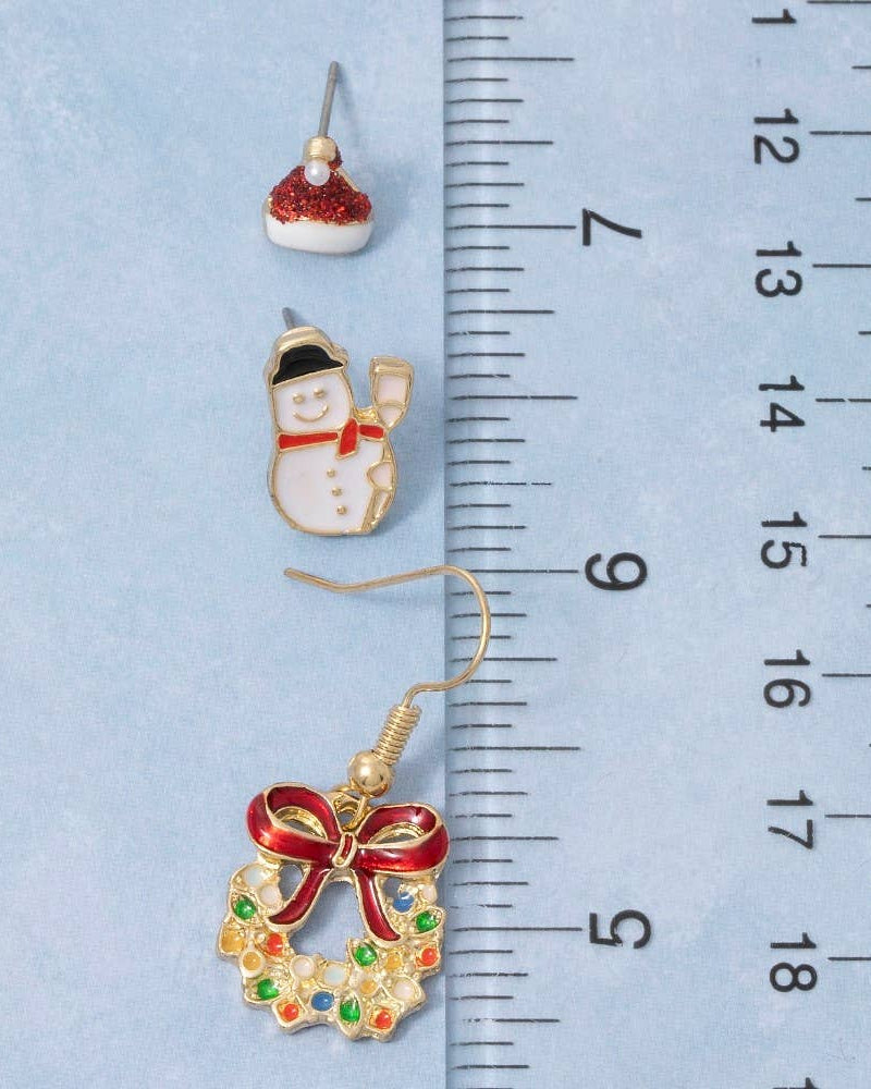 Two Christmas-themed earrings next to a ruler on a light blue background
