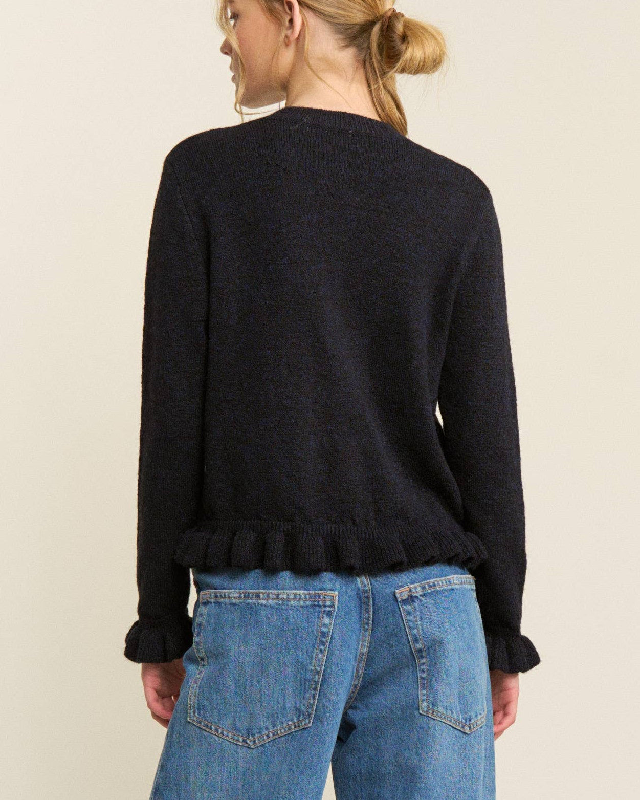 Person wearing a black sweater and blue jeans on a plain background
