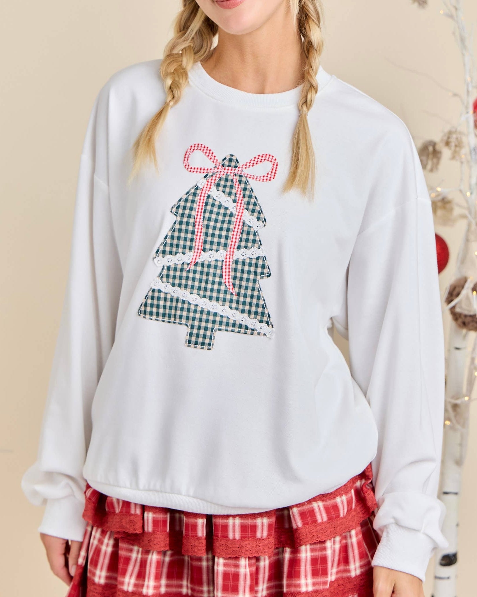 White sweatshirt with a Christmas tree design worn by a person, with a neutral background.