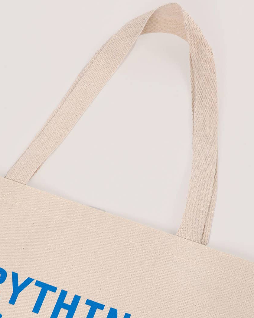 Beige tote bag with blue text on a light gray background