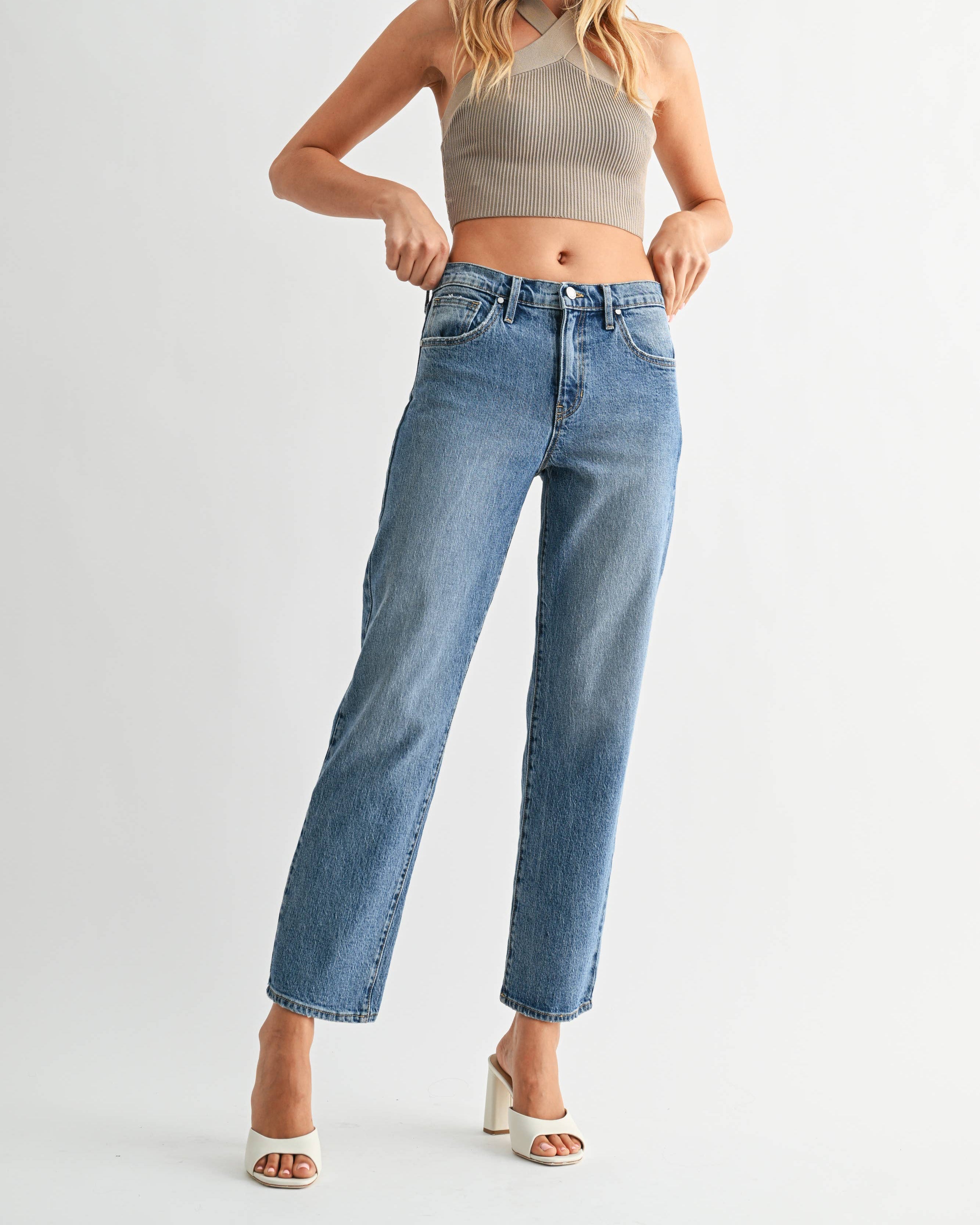 Woman wearing a beige crop top and blue jeans on a white background