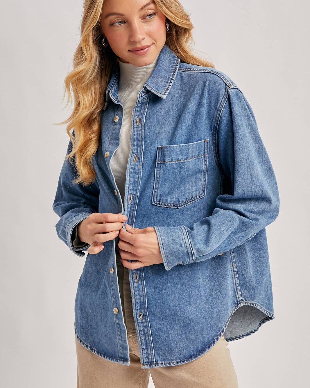 Woman wearing a blue denim shirt over a white sweater on a light gray background