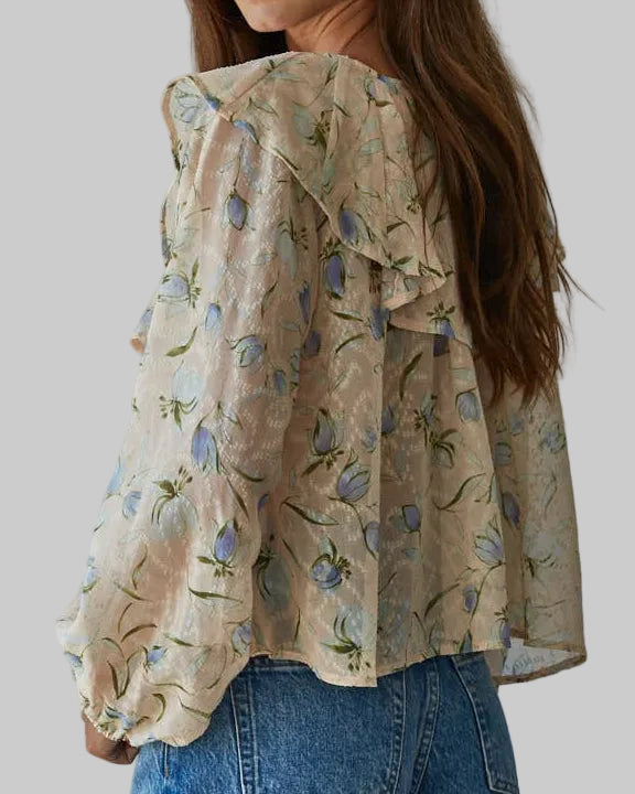 Woman wearing a floral blouse with ruffled sleeves against a plain background