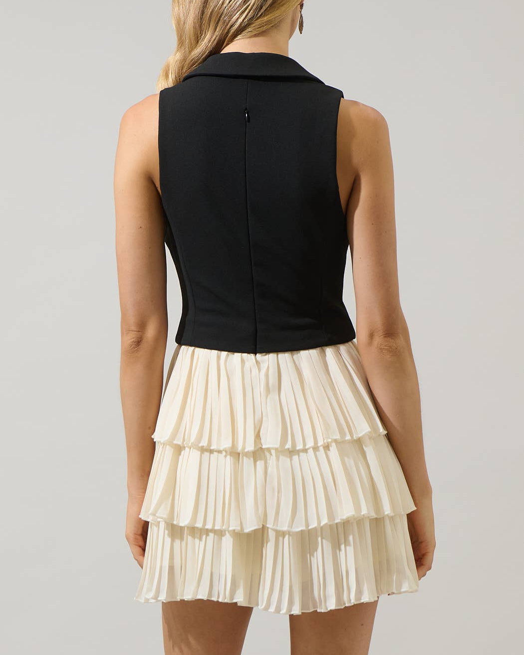 Woman wearing a black sleeveless top and cream ruffled skirt on a gray background