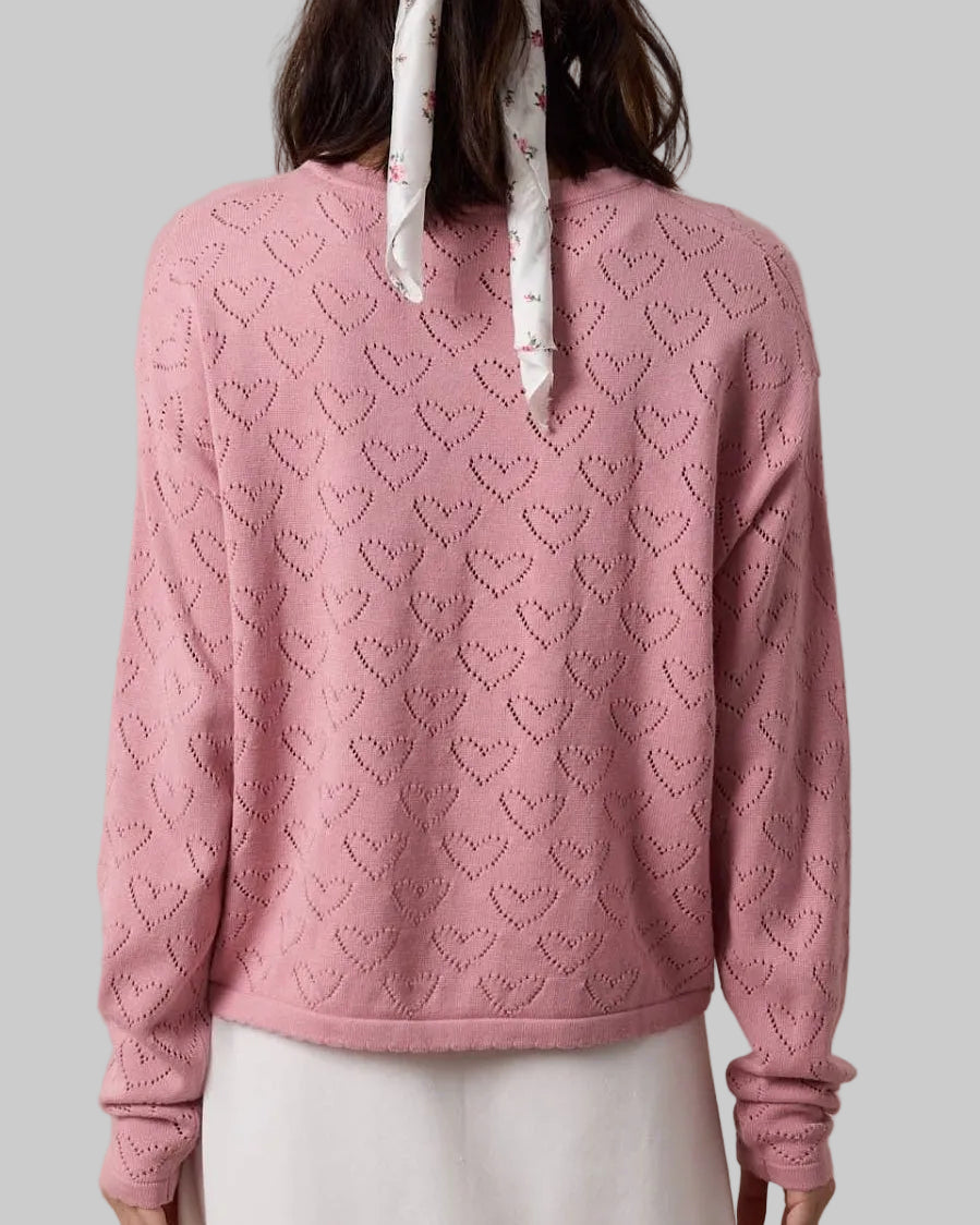Person wearing a pink sweater with a subtle pattern, standing against a beige background