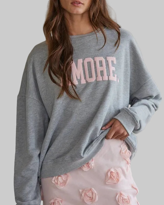 Woman wearing a gray sweatshirt with 'MORE' in pink and a patterned skirt.