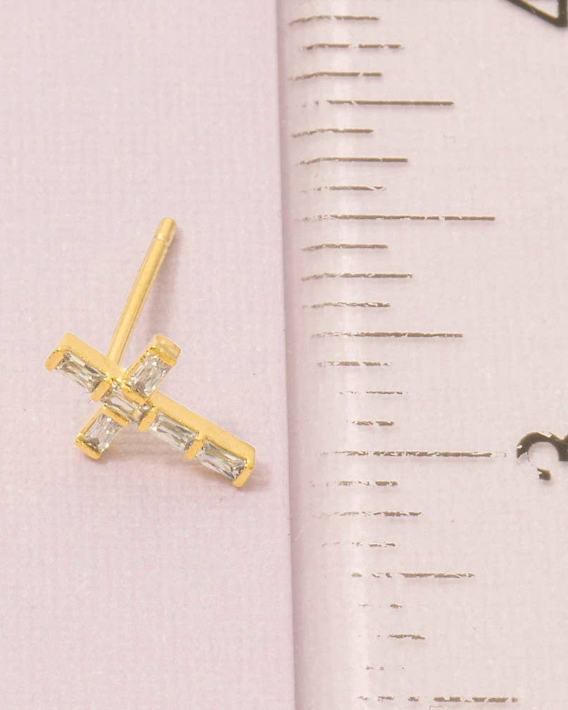 Gold cross-shaped earring next to a ruler on a pink background