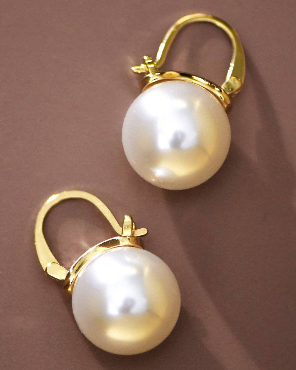 Pair of pearl earrings with gold clasps on a brown background