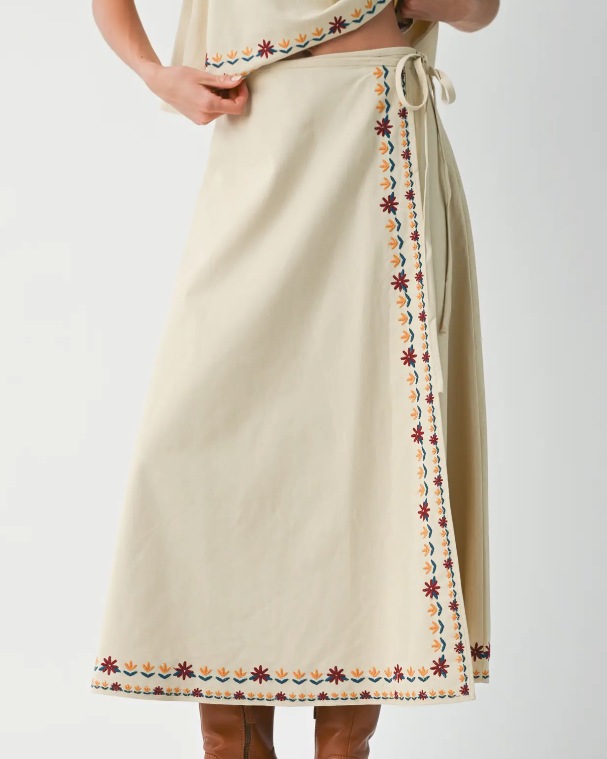 Beige skirt with decorative trim worn by a person on a light gray background