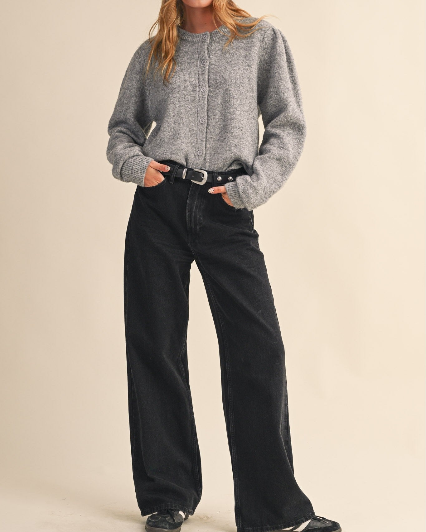 Woman wearing a gray sweater and black pants with a beige background