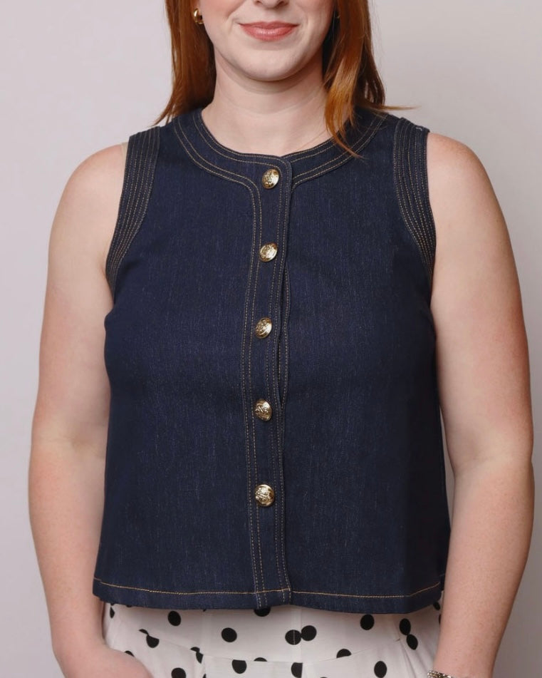 Person wearing a dark denim vest with gold buttons on a plain background