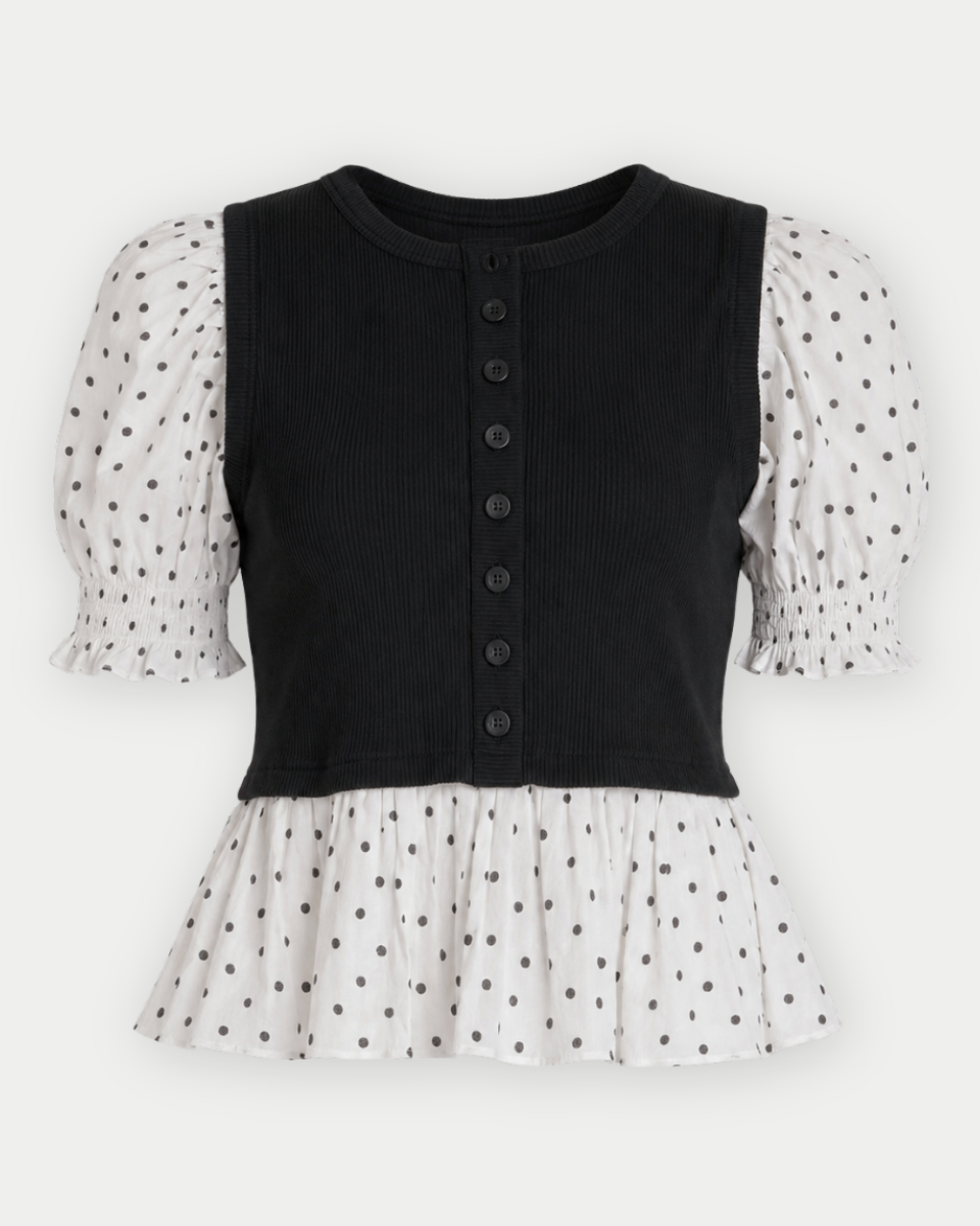 A women's knit top with a black ribbed vest-style bodice and button-front closure, paired with white puff sleeves and a white ruffled hem featuring black polka dots, shown on a light gray background.