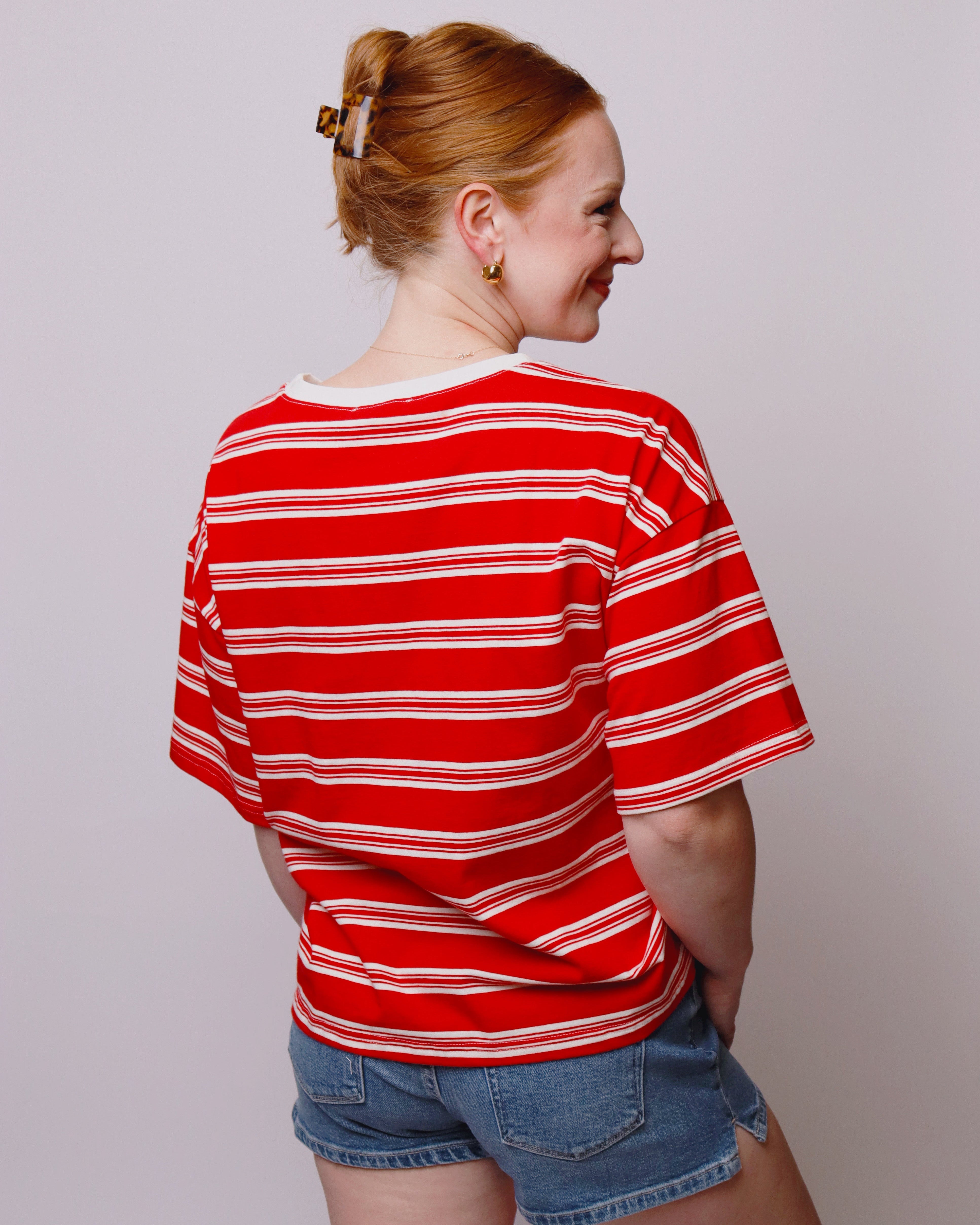 Person wearing a red and white striped shirt and denim shorts against a plain background