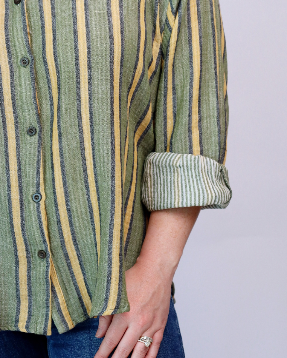 Close-up of a person wearing a striped button-up shirt with rolled sleeves and blue jeans against a plain light background.