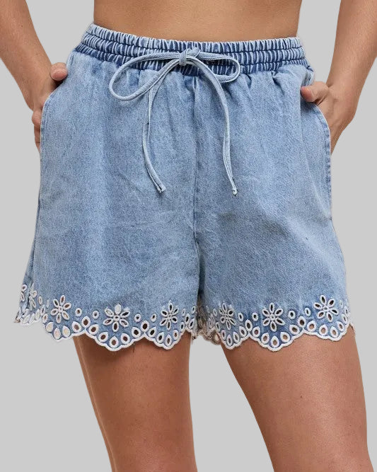 Model wearing light denim shorts with embroidery detail on a neutral background