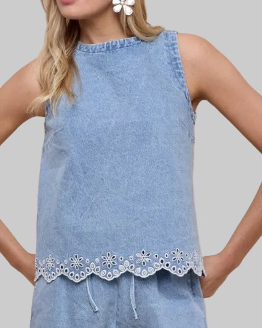 Model wearing a light blue sleeveless denim with eyelet embroidery at hem top on a neutral background. Front view