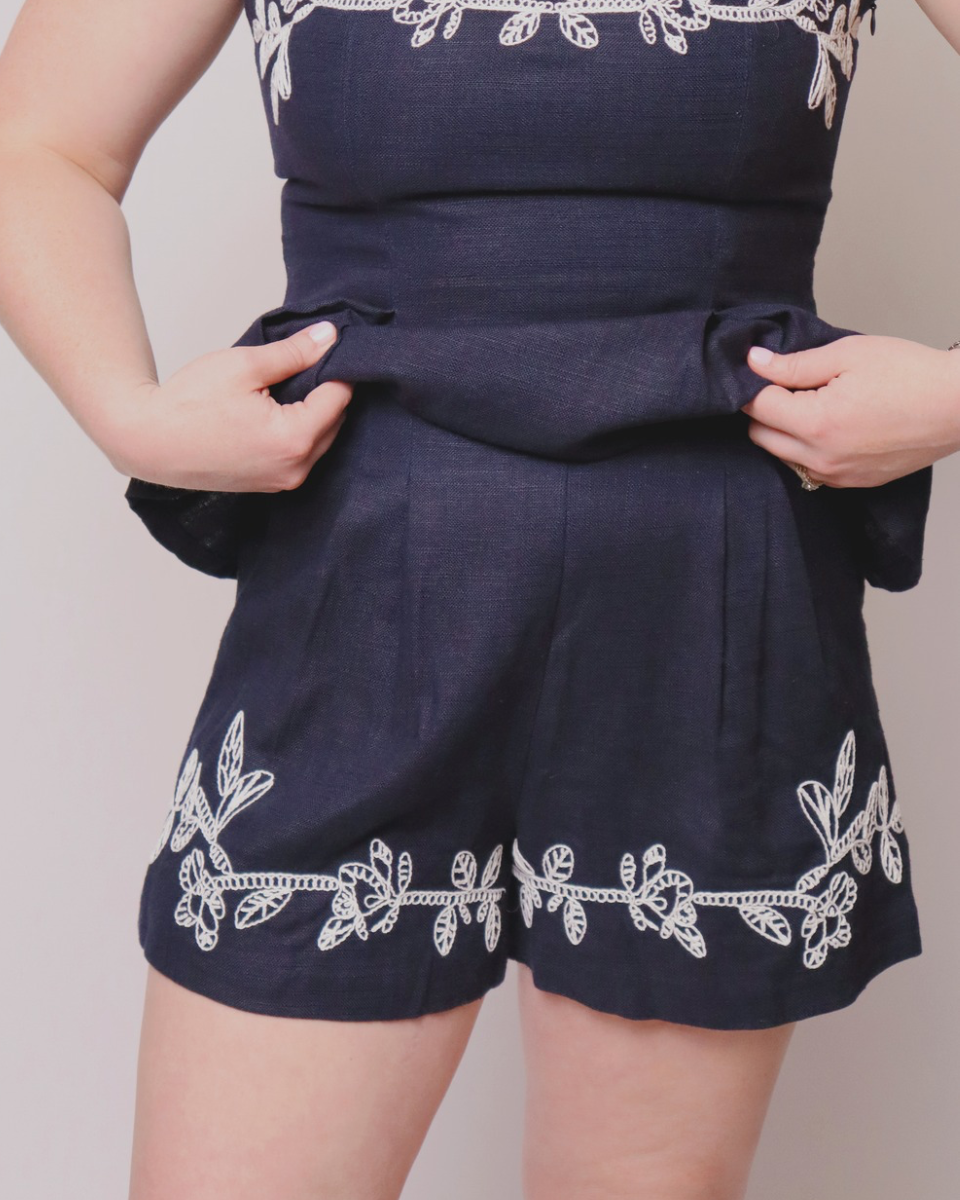 Navy blue romper with white embroidery on a plain background