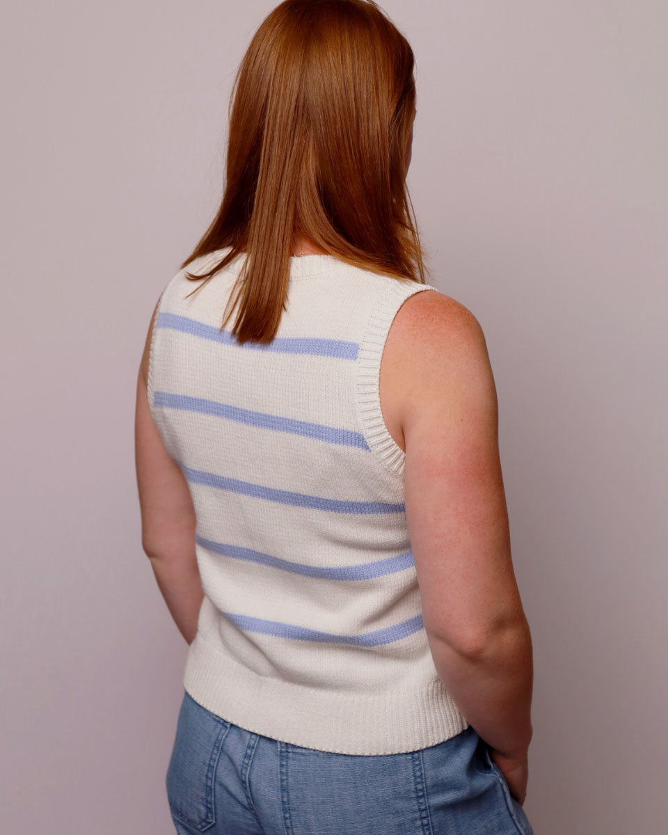 Person wearing a sleeveless sweater with blue stripes on a plain background