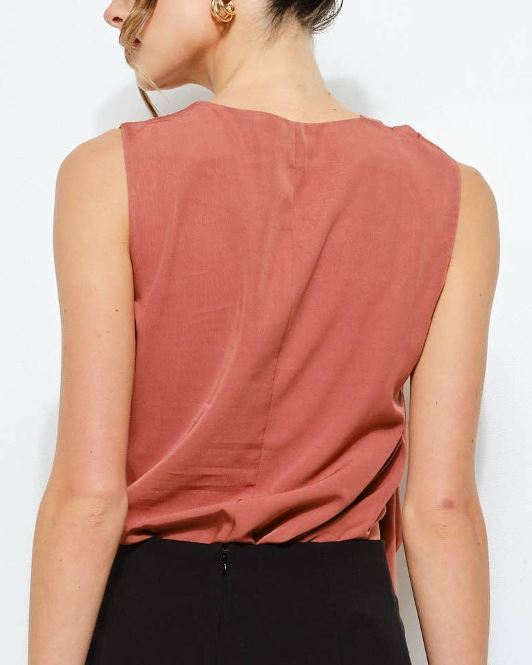 Woman wearing a sleeveless rust-colored top and black skirt on a white background