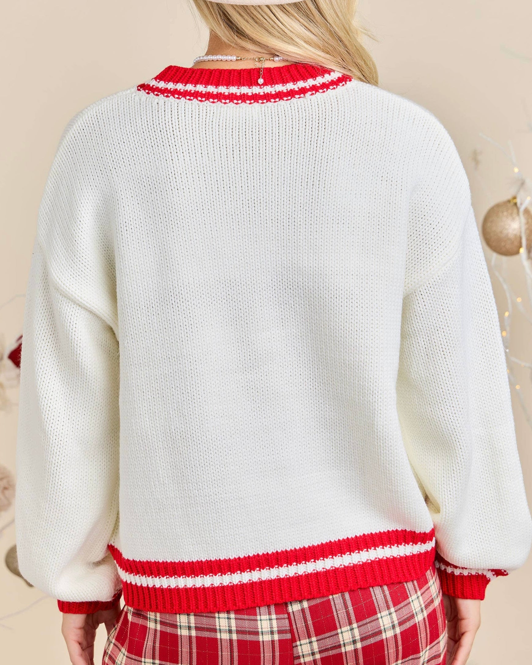 White sweater with red trim worn by a person, on a beige background