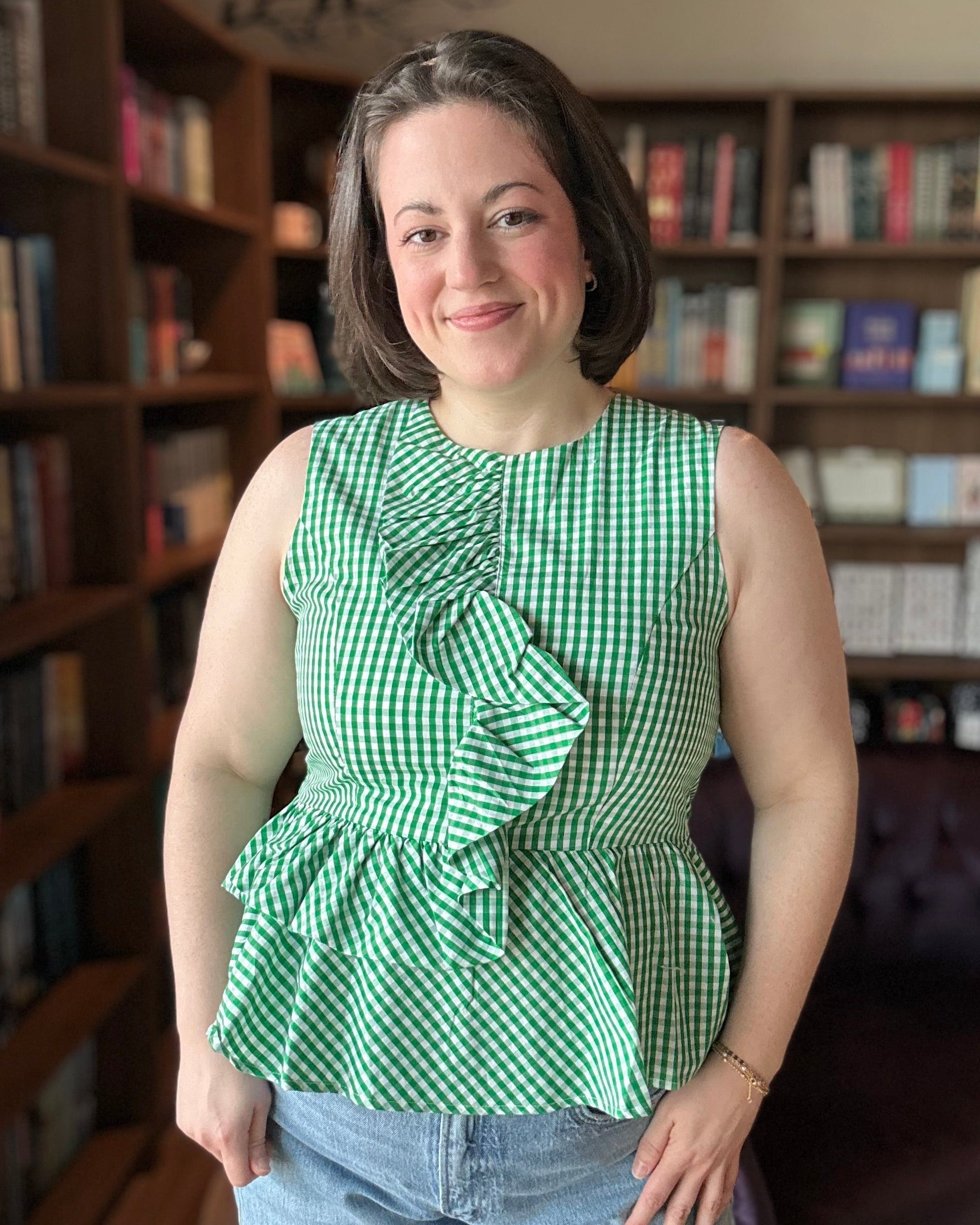 Woman wearing a green checkered top with ruffles in a room with bookshelves.