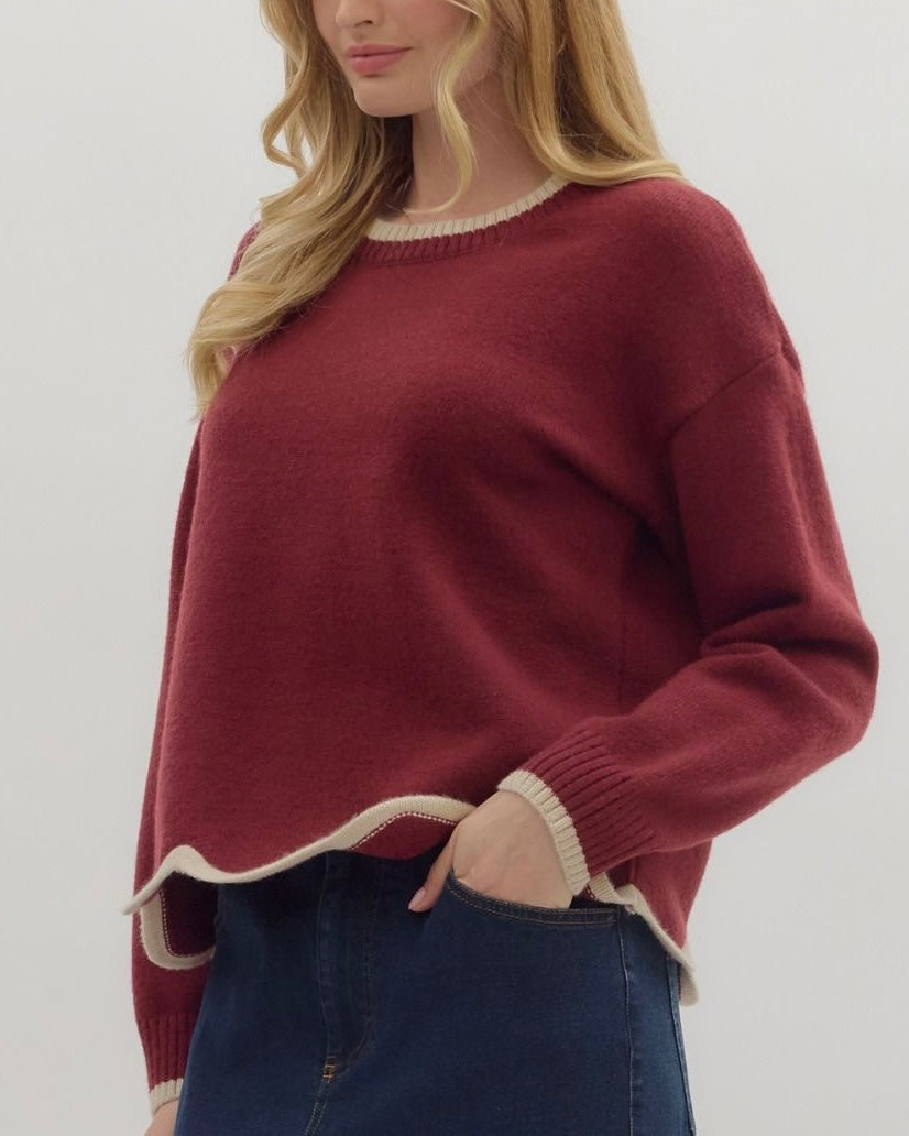 Person wearing a maroon sweater with white trim on a plain background