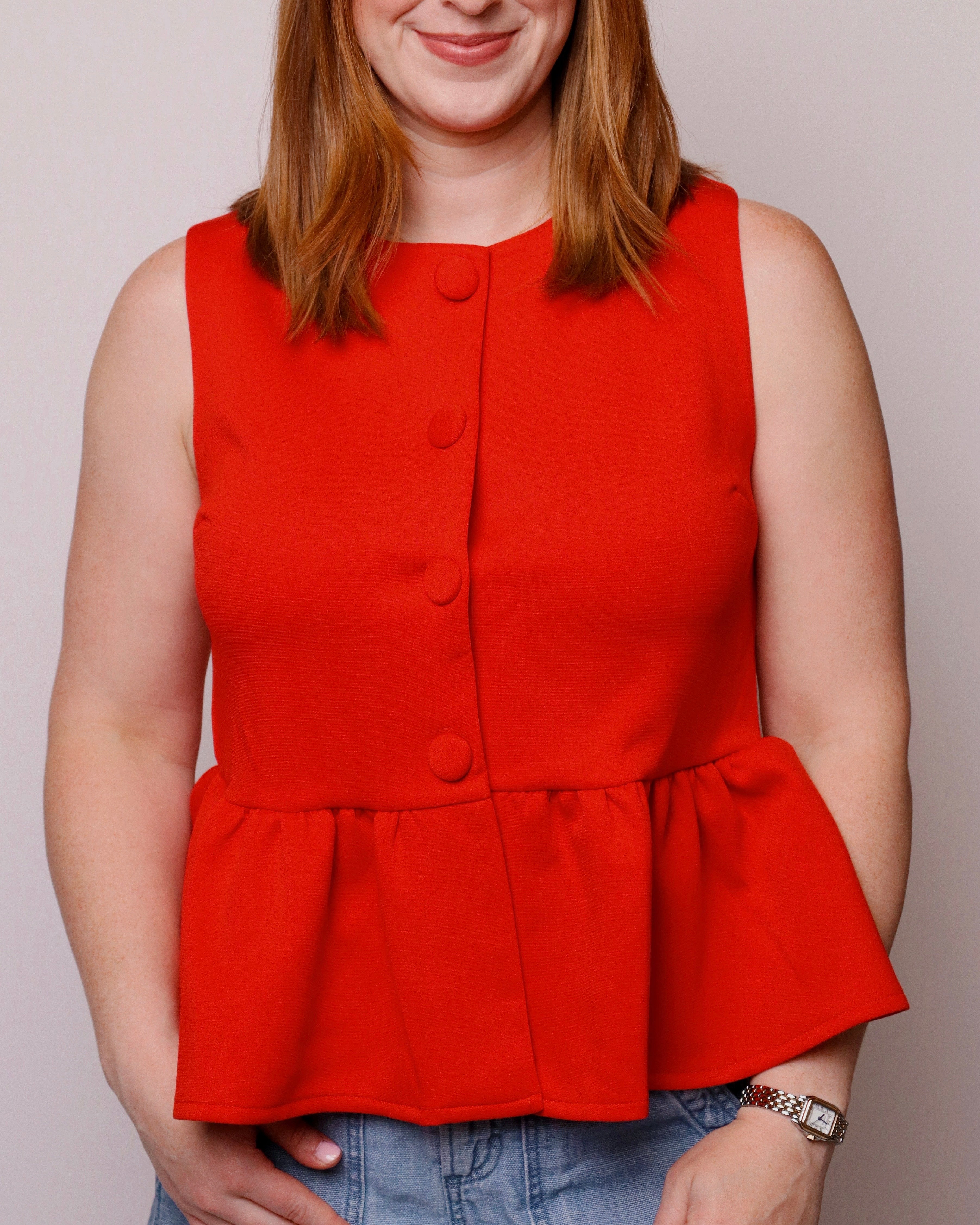 Person wearing a red peplum top against a plain background
