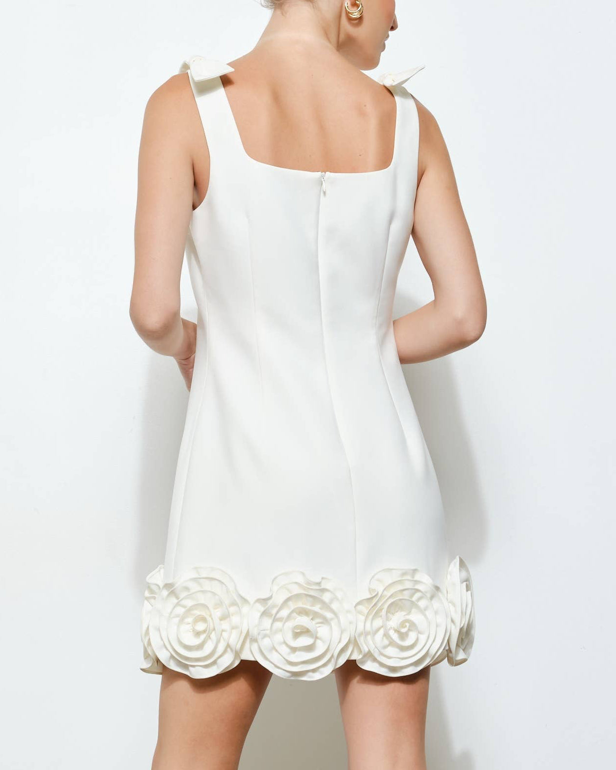 Woman wearing a white dress with floral details on a plain background