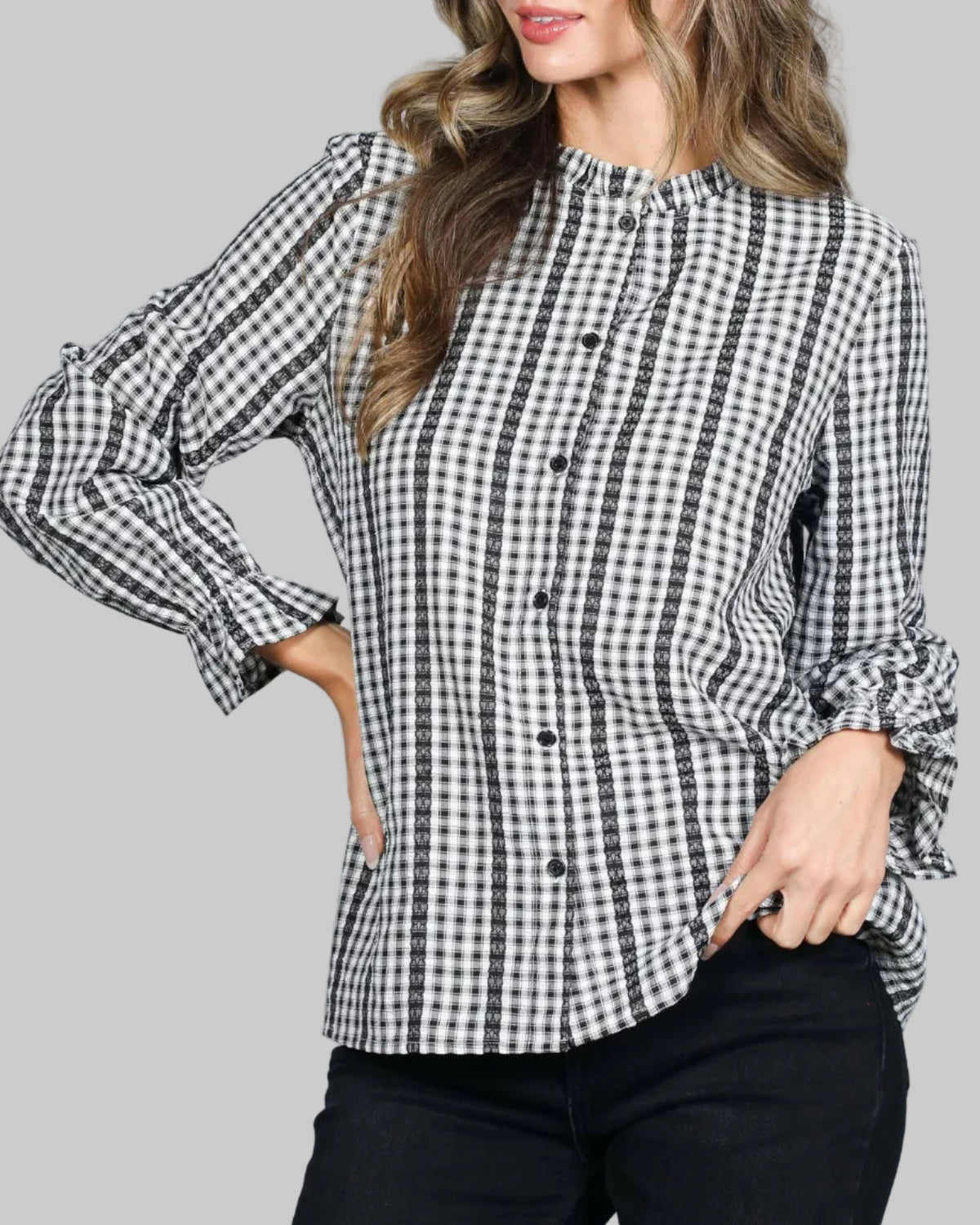 Model wearing a black and white gingham button up top. Ruffled neckline and elasticized long sleeves