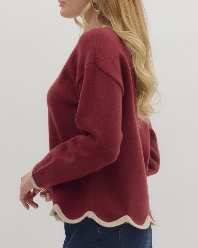 Person wearing a maroon sweater with scalloped hem on a plain background