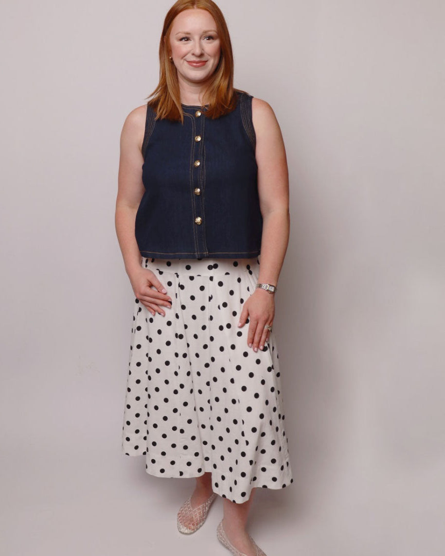Woman wearing a sleeveless navy top and polka dot skirt against a plain background