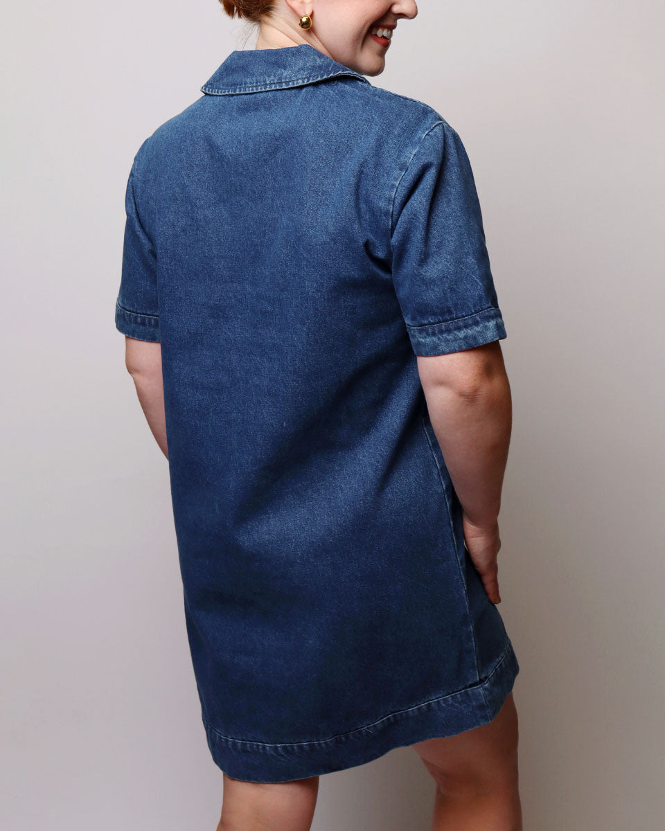 A woman wearing a short-sleeve denim shirt dress, shown from the back against a plain light gray studio background.