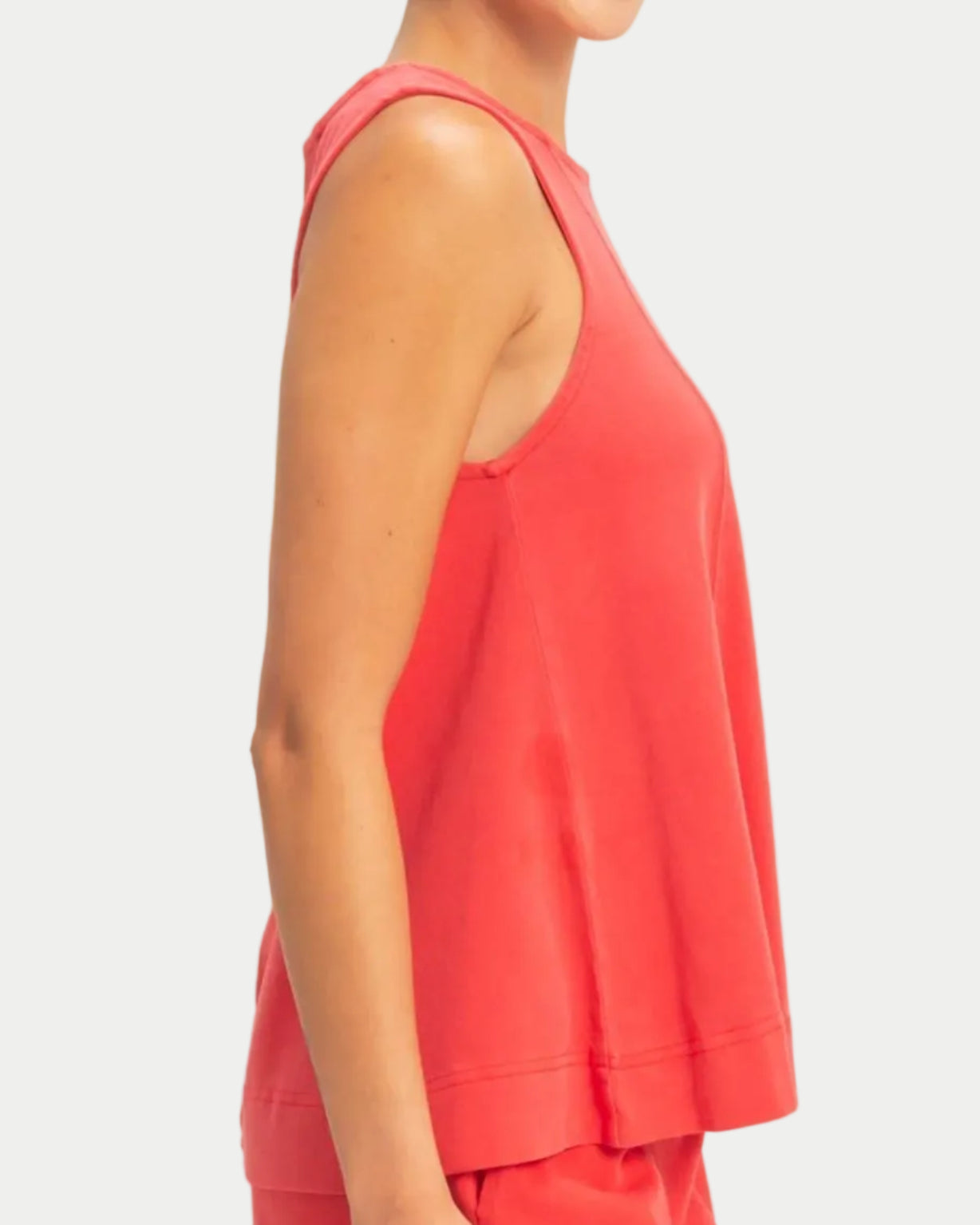 Woman wearing a red sleeveless swing top on a neutral background. side view