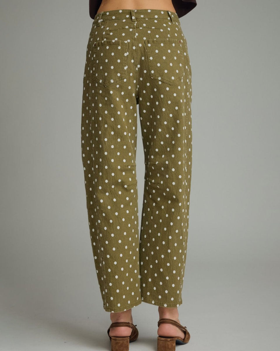 A person shown from the back wearing olive green cropped pants with a white polka dot pattern, paired with brown heeled sandals against a plain gray studio background.