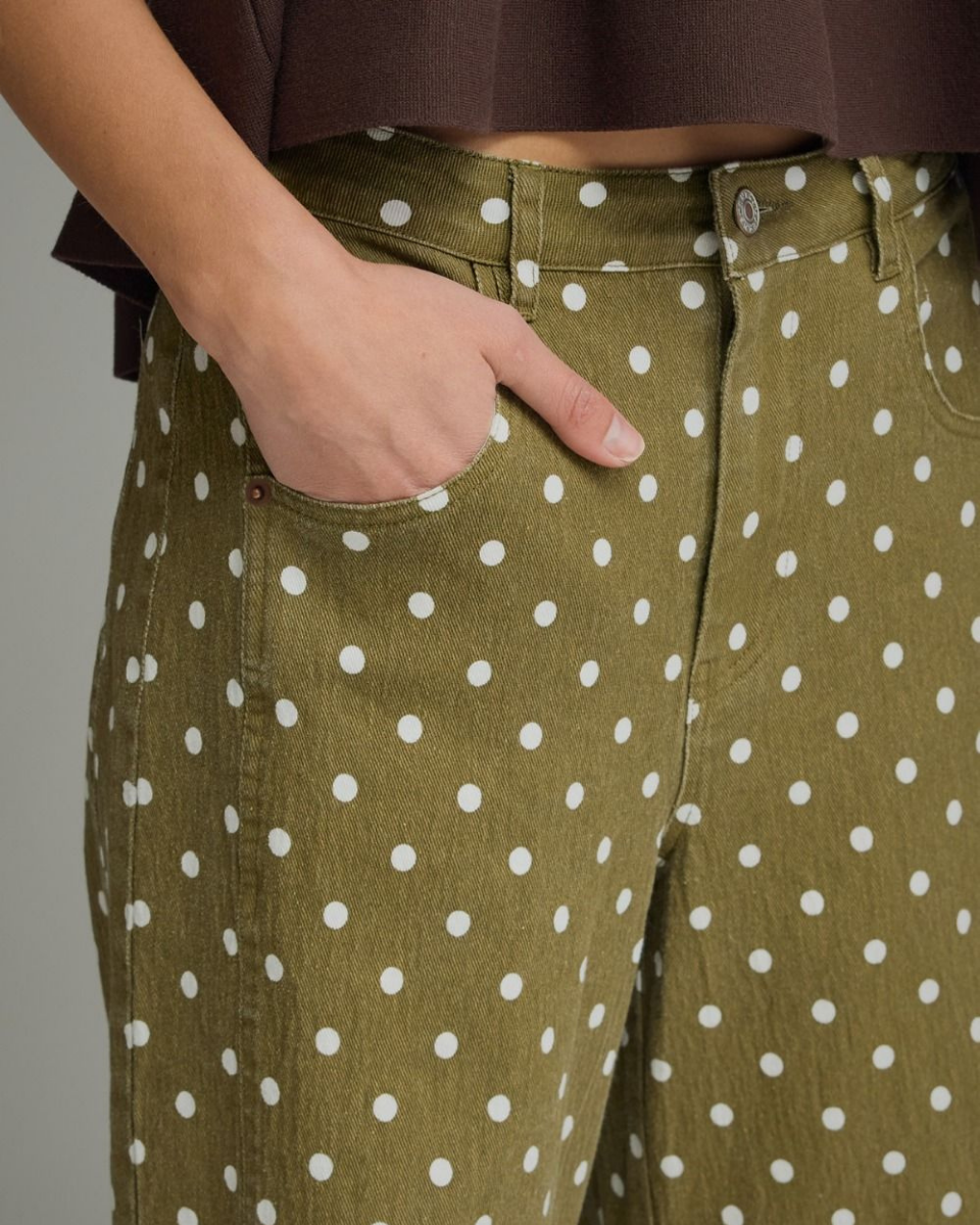Close-up of olive green wide-leg pants with a white polka dot pattern, worn by a model with a hand in the pocket.