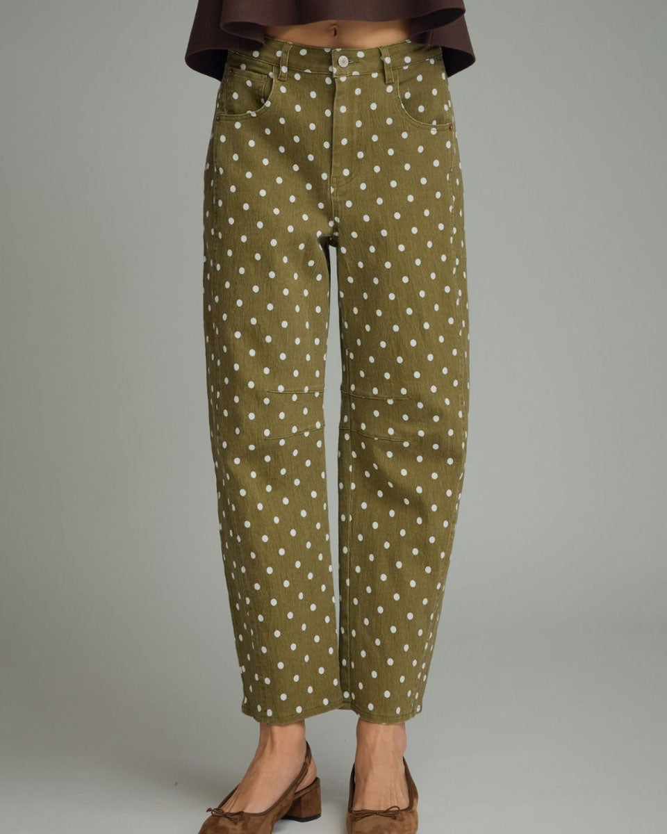 A person wearing olive green cropped pants with a white polka dot pattern, paired with brown shoes, shown from the waist down against a plain gray studio background.
