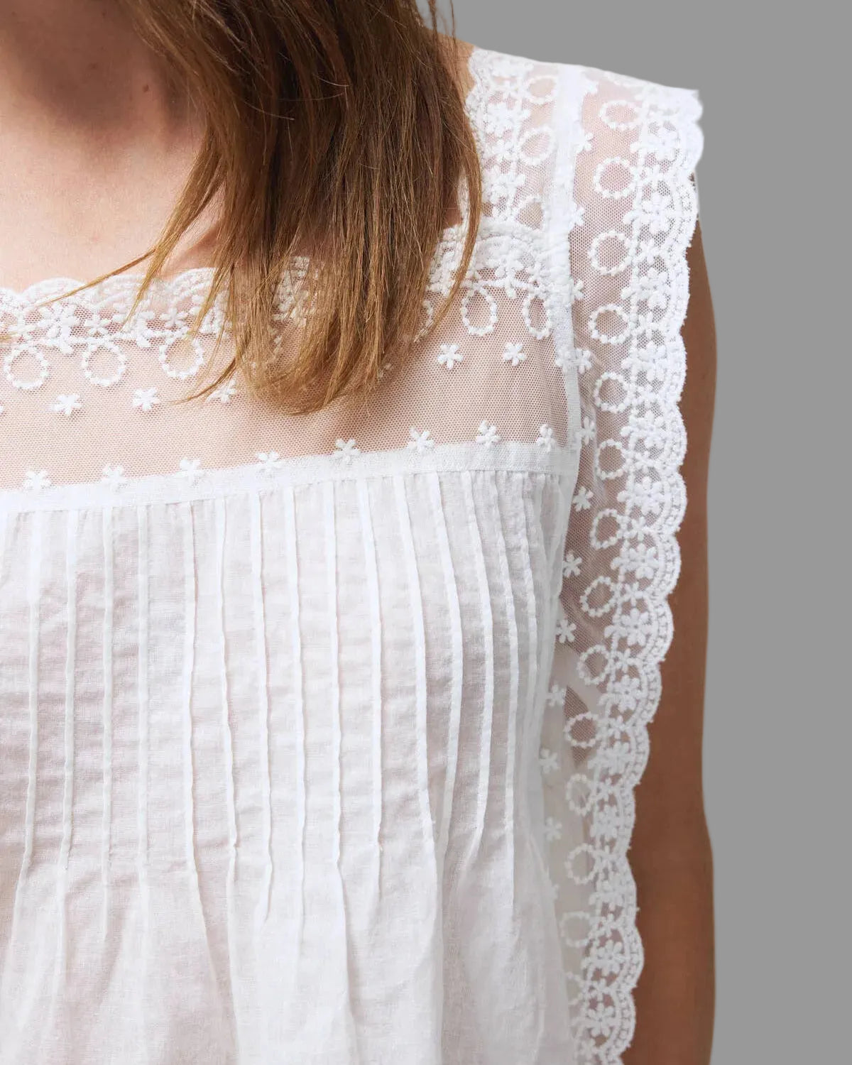 Model wearing the Daisy white lace top on a neutral background lace top on a plain background close up view