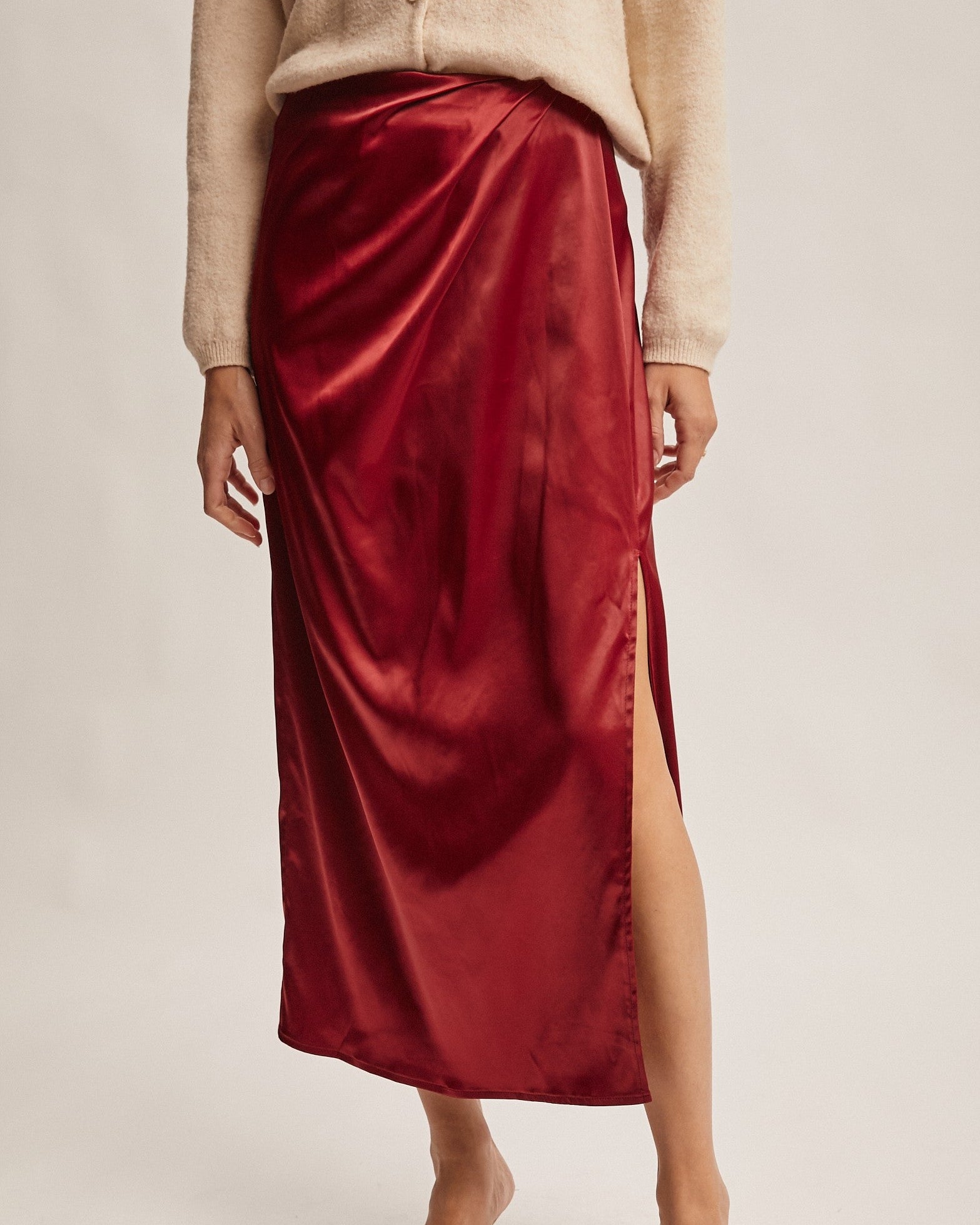 Person wearing a red satin skirt with a beige top and shoes on a neutral background