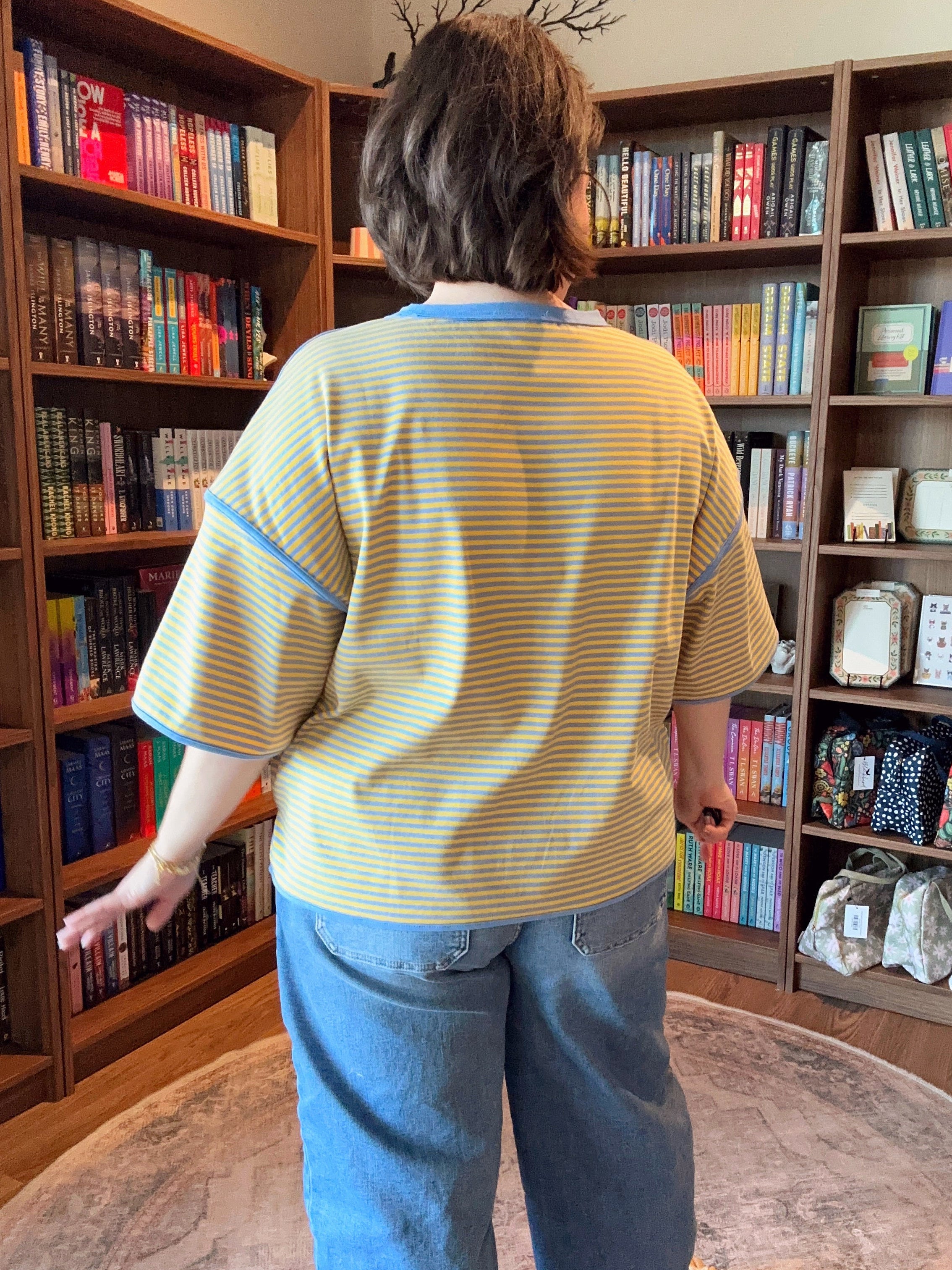 Person standing in a room with bookshelves filled with books and decorative items.