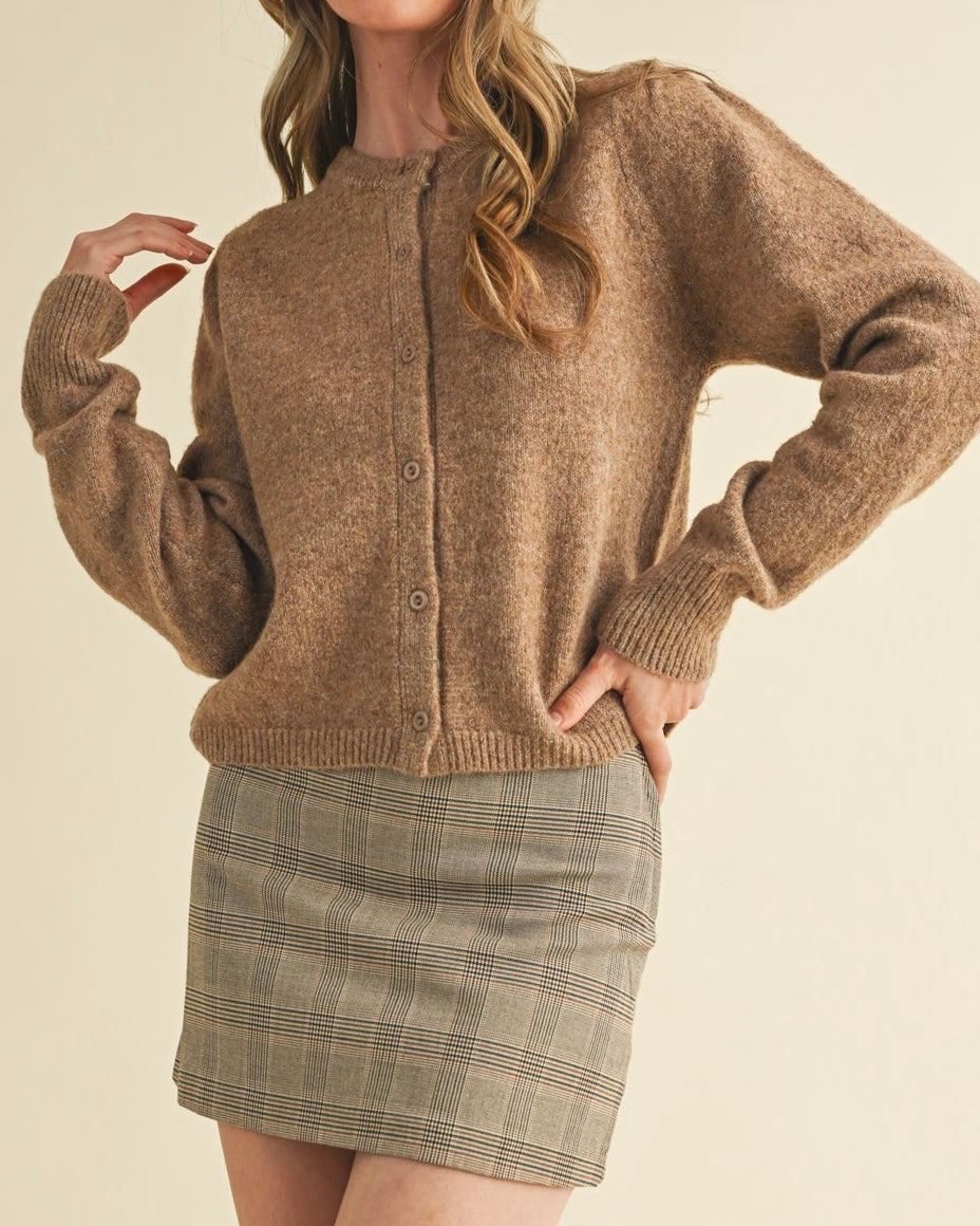 Person wearing a brown cardigan and plaid skirt on a beige background