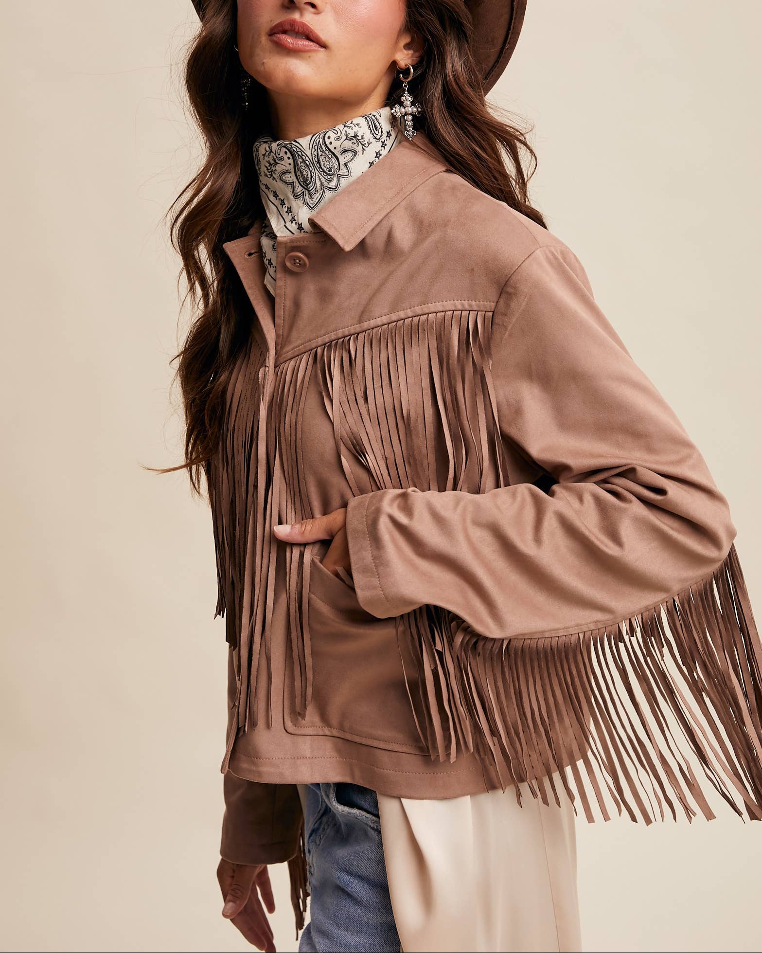 Woman wearing a brown fringed jacket and hat against a beige background
