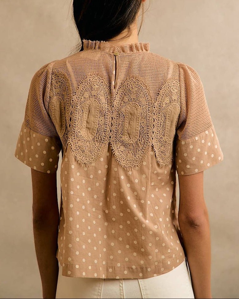 Model wearing a beige blouse with polka dots and lace details against a neutral background