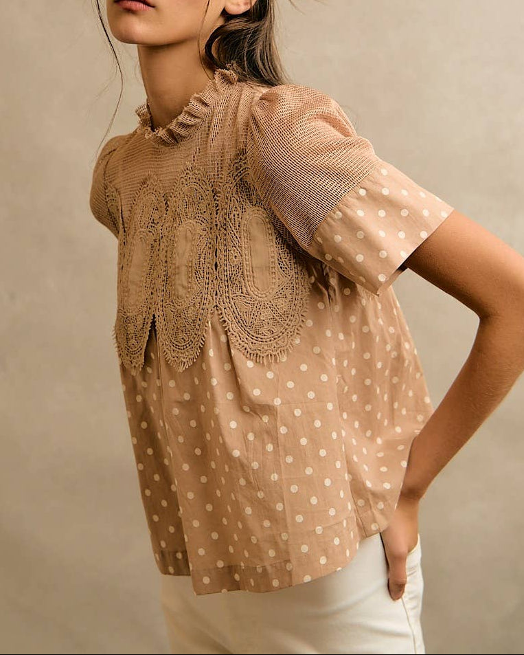 Model wearing a beige blouse with polka dots and lace details against a neutral background side angle