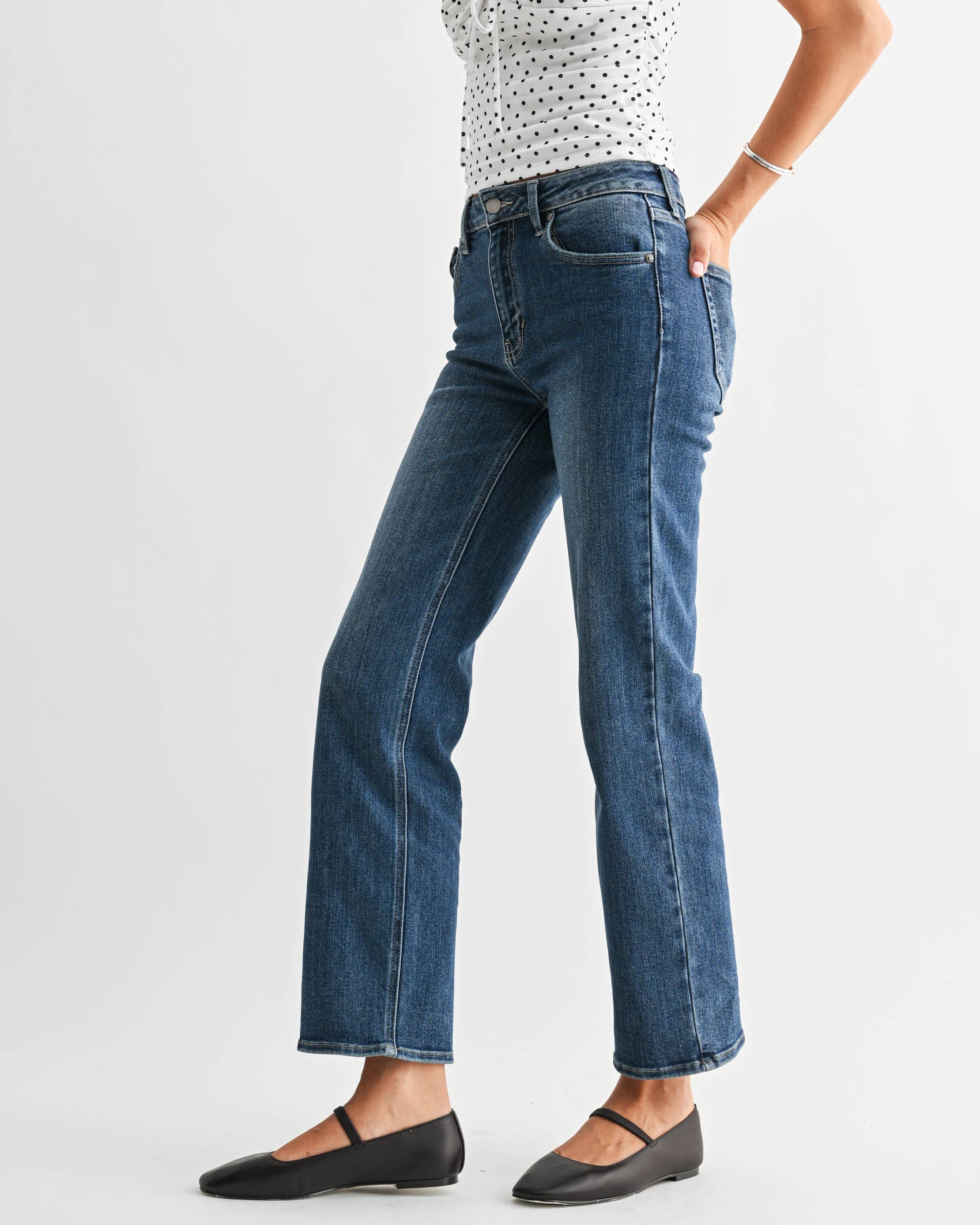 Woman wearing a white sleeveless top with black polka dots and blue jeans on a white background