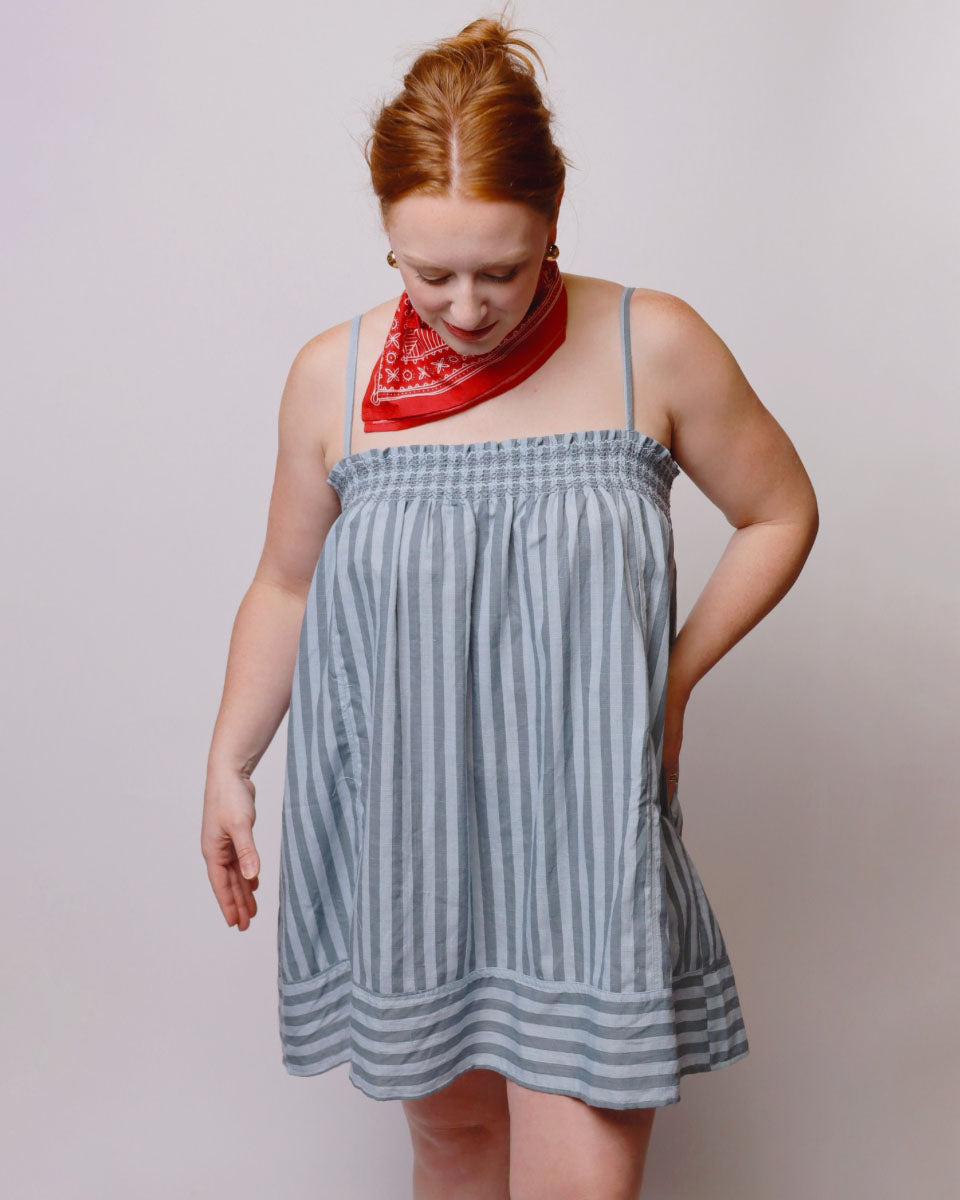 Woman wearing a blue and white striped dress with a red bandana on a plain background